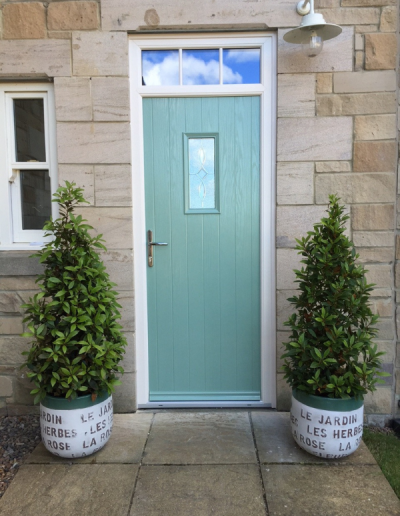 teal entrance door with 2 small bushes either side of the light bricked home