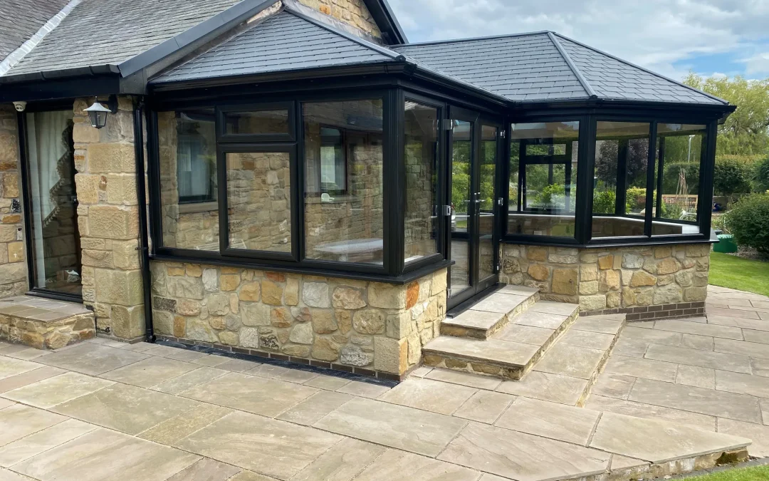 Refurbished conservatory with a solid tiled warm roof and black frames on a stone bungalow